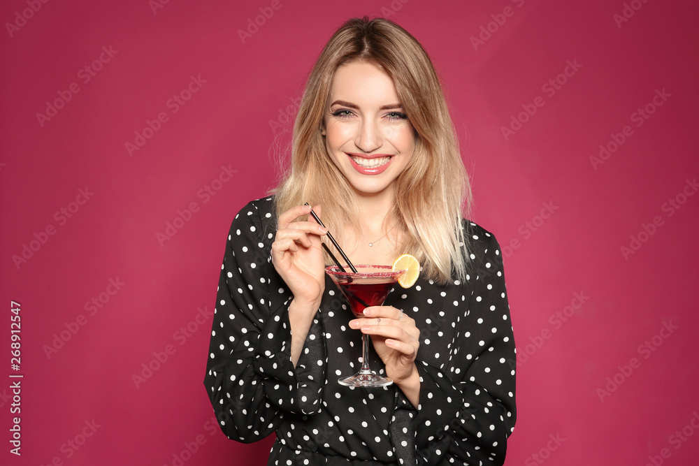 Wall mural Beautiful young woman with glass of martini cocktail on color background