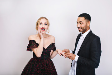 Portrait handsome joyful man in white shirt making proposal of marriage to attractive astonished young woman in luxury evening dress on white background. Celebration, valentines, lovers, together
