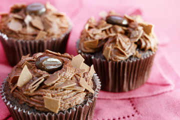 brown cupcakes with cocoa butter cream and chocolate chips on a pink tablecloth, close up shot, selected focus, narrow depth of field