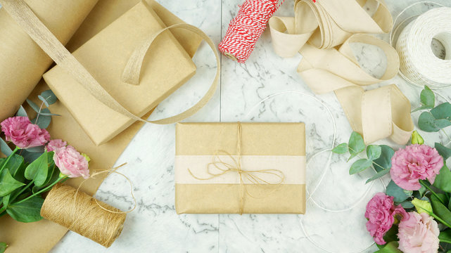 Zero-waste gift wrapping flatlay overhead with kraft paper, jute and natural cotton ribbons and garden flowers for eco-friendly lifestyle.