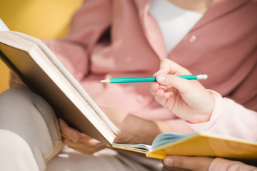 partial view of child pointing with pencil at book in mothers hands