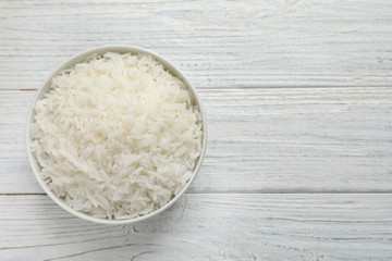 Bowl of tasty cooked rice on white wooden background, top view. Space for text