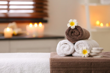 Composition with towels, flowers and stones on massage table in spa salon. Space for text
