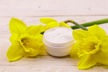 Obraz na płótnie Canvas Jar of moisturizer cream with yellow daffodils on white wooden background