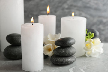 Fototapeta na wymiar Burning candles, spa stones and flowers on table. Space for text