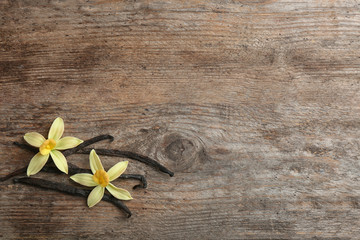 Flat lay composition with vanilla sticks and flowers on wooden background. Space for text