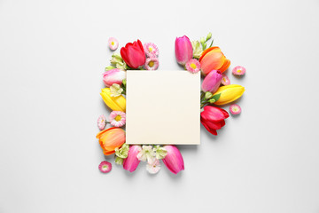 Beautiful composition with spring flowers and blank card on white background, top view. Space for text