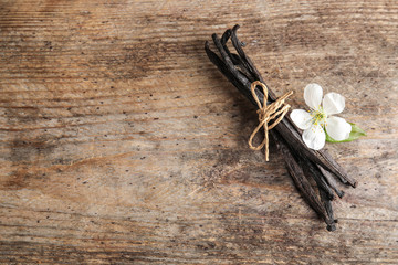 Flat lay composition with aromatic vanilla sticks and flower on wooden background. Space for text