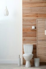Toilet bowl near wooden wall in modern bathroom interior