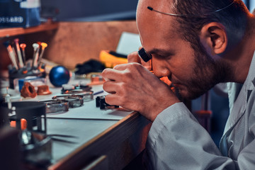 Focused pensive master is working on client's watch at his workshop.