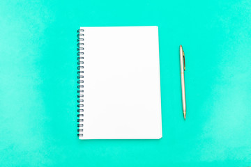 White notepad with steel pen on a green background. Office table, minimal composition. Copy space.