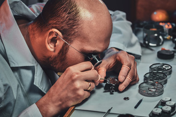 Undistracted clockmaster is fixing old watch for a customer at his own workshop.