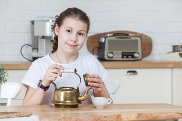Twelve years old girl holding teapot with opened cap in hands, looking at camera, kitchen interior