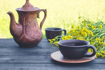 A teapot and a cup of tea stand on wooden old boards with yellow daisy flowers. With copy space.