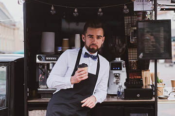 Attractive elegant barista is drinking coffee while waiting for customers at his own small coffeeshop.