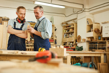 Waist up portrait of senior carpenter teaching apprentice  while working  in joinery workshop, copy...