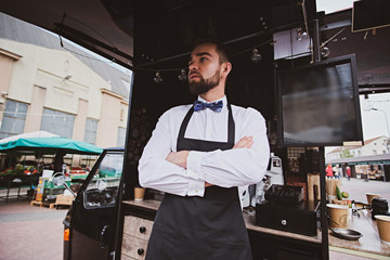 Handsome elegant barista is standing crossed his hands next to his coffeeshop.