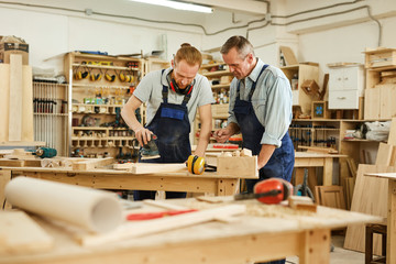 Portrait of senior carpenter teaching apprentice  while working  in joinery workshop, copy space
