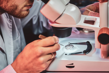Mature clockmaster is fixing old watch for a customer at his busy repairing workshop.