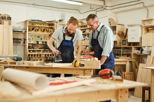 Portrait of senior carpenter teaching apprentice while working in joinery workshop, copy space