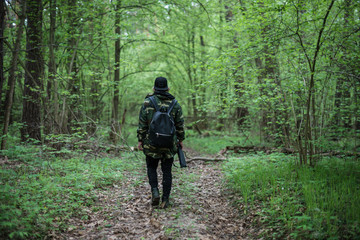 A young man in a camouflage jacket is walking along a forest path, view from the back
