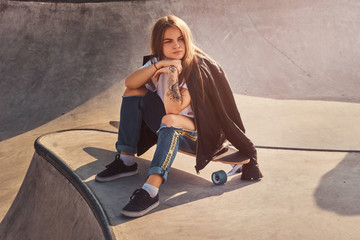 Trendy young woman with long hair is sitting at skatepark on her longboard. © Fxquadro