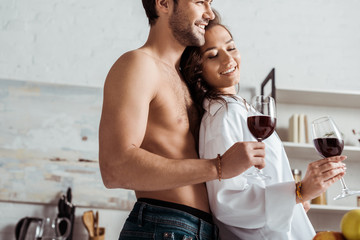 low angle view of happy muscular man holding wine glass near attractive and happy girl at home
