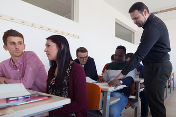 Male professor explain lesson to students and interact with them in the classroom.Helping a students during class. University student being helped by male lecturer during class.