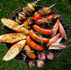 Grilled food, pork sausages, baguette toasts and onion on  grill plate, outdoors, top view. Barbecue, bbq