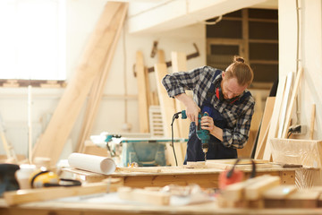 Waist up portrait of red haired carpenter working in joinery lit by sunlight, copy space