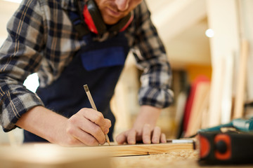 Mid section portrait of modern carpenter marking wood while working in joinery lit by sunlight, copy space