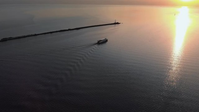 Follow white ship yacht - Aerial sunset top Lighthouse view with ships in the background - Warm setting sun landscape scenery during Golden Hour