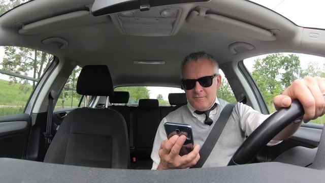 People, travel and communication technology. Man with mobile telephone driver with cell phone, driving car on the street, using smartphone for text messaging and internet. Danger and risk on the road