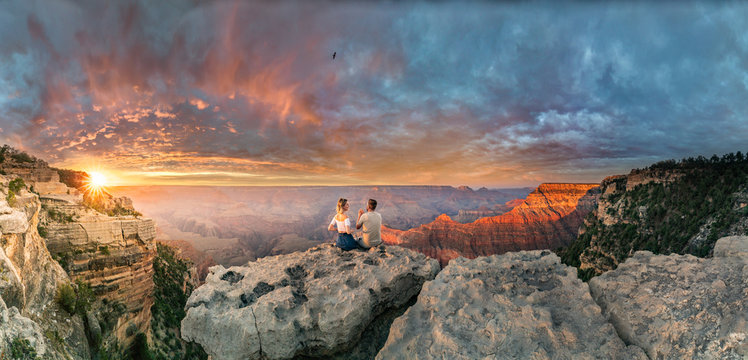 Man and woman sit on the edge of rim talking about future and watching the Grand Canyon sunset while bird in the sky