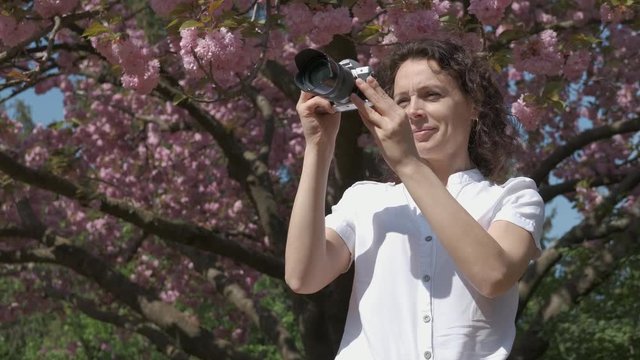 Woman photographer in the park. Female photographer against the background of blooming sakura.