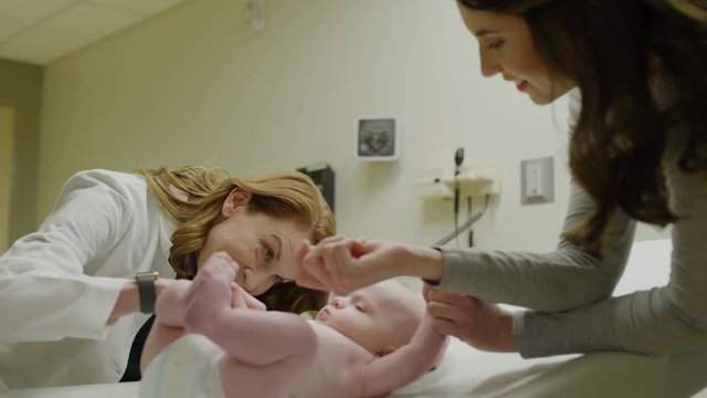 Low angle view of doctor with otoscope examining ear of baby with mother watching / Salt Lake City, Utah, United States
