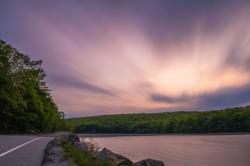 Dramatic sky over the lake at Harriman State Park, upstate New York, featuring road passing through the forest on the foreground. Shot using slow shutter speed