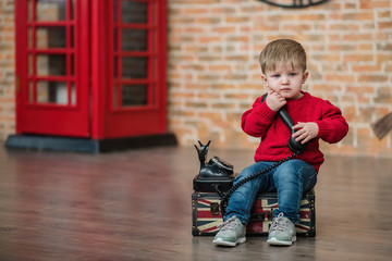 A little boy is talking on the phone near a red English phone booth. Language centre. Traveling around the world.