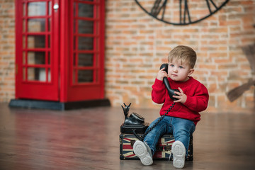 A little boy is talking on the phone near a red English phone booth. Language centre. Traveling around the world.