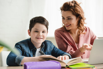 cheerful mother with adorable son doing schoolwork together at home