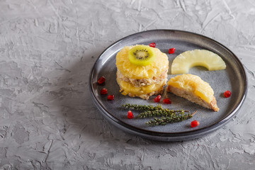 Pieces of baked pork with pineapple, cheese and kiwi on gray plate.