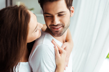 attractive girl hugging happy man standing in white t-shirt at home