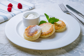 cheesecakes from cottage cheese with sour cream on white plate