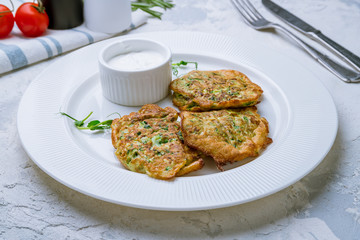 Fried zucchini pancakes with sour cream on white plate