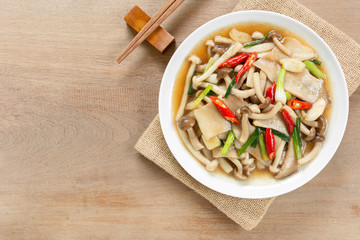 top view of stir fried mixed mushroom with soy sauce in a ceramic dish on wooden table. asian homemade style food concept.