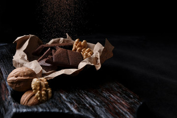 broken chocolate on paper on a black board on a dark background with walnut