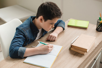 high angle view of attentive boy writing in copy book while doing schoolwork at home