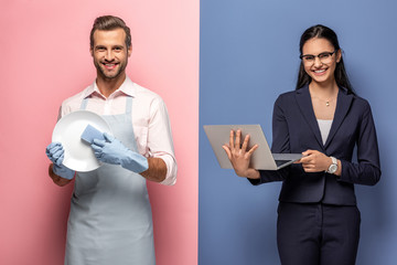 man in apron washing plate while businesswoman using laptop on blue and pink