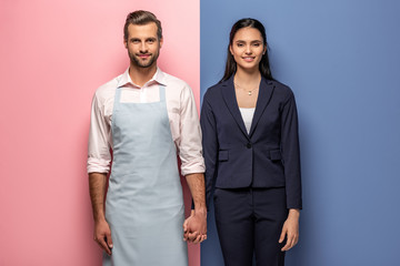 smiling man in apron and businesswoman holding hands on blue and pink