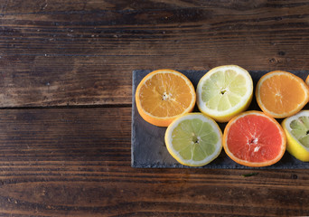 Fototapeta na wymiar Sliced lemons and oranges cut on a slate board, on a wooden table